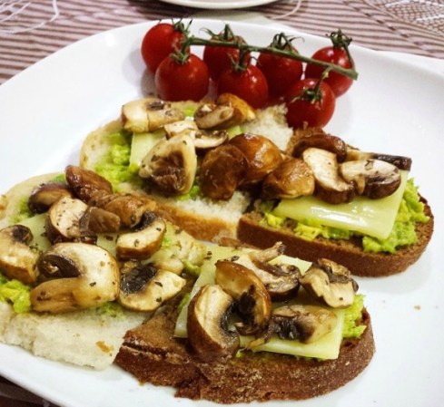 Pan tostado con aguacate, champiñones y jitomates cherry.