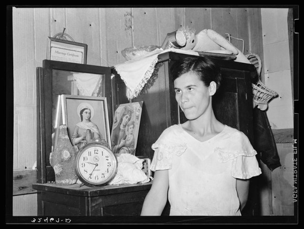 Mujer mexicana de pie delante de una cómoda con imágenes religiosas. San Antonio, Texas.