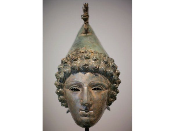 La superficie pulida y blanca que lució un día la parte del rostro de la máscara, debía contrastar con el bronce del pelo y el "gorro frigio" que conformaban la parte del casco.