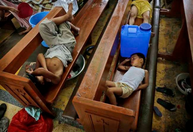 TACLOBAN, PHILIPPINES - NOVEMBER 13: Residents take shelter in a church in the aftermath of Typhoon Haiyan on November 13, 2013 in Tacloban, Leyte, Philippines. Typhoon Haiyan, packing maximum sustained winds of 195 mph (315 kph), slammed into the southern Philippines and left a trail of destruction in multiple provinces, forcing hundreds of thousands to evacuate and making travel by air and land to hard-hit provinces difficult. Around 10,000 people are feared dead in the strongest typhoon to hit the Philippines this year. (Photo by Kevin Frayer/Getty Images)