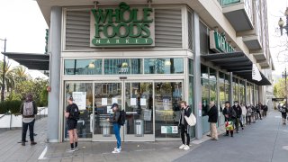 Customers, some wearing protective masks, wait in a line outside a Whole Foods Market Inc. store in San Francisco.