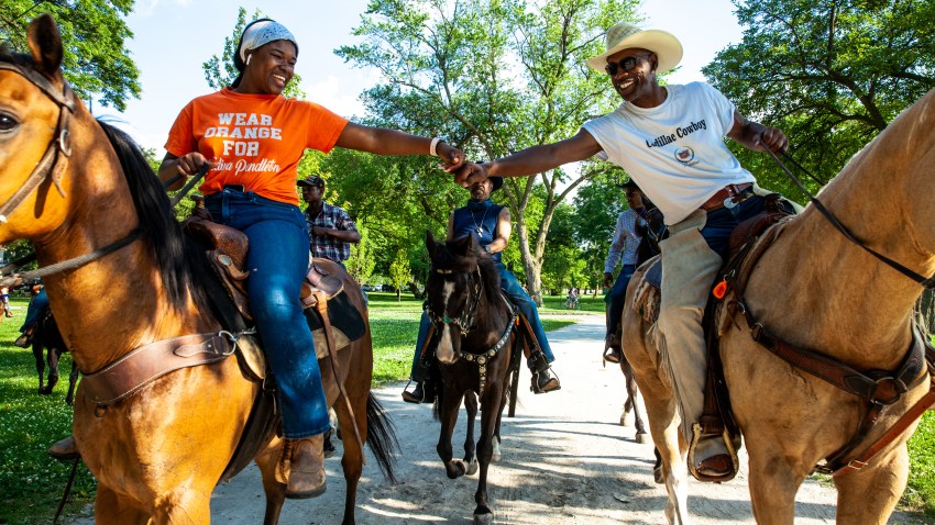 Two black riders on horseback fist bump in front of some trees