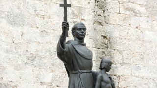 Statue of Junipero Serra holding a cross and the shoulder of an indigenous boy