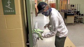 A custodian wipes down a hallway doorway at the Mildred Avenue K-8 School building in Boston's Mattapan and for the reopening of school on July 9, 2020.