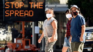 Pedestrians in masks walk in front of a sign reminding the public to take steps to stop the spread of coronavirus, July 23, 2020, in Glendale, Calif.