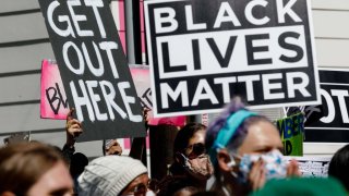 Protesters hold banners reading "Get Out Here" and "Black Lives Matter" during a demonstration led by the NAACP