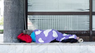 An unhoused person sleeping on the floor outside a building