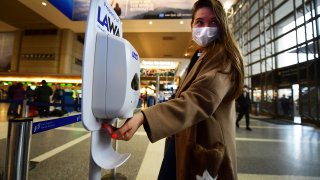 A woman wearing a facemask uses hand sanitizer on arrival at LAX.