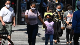 People wearing masks walk on a street in downtown Los Angeles.