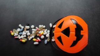Plastic Pumpkin basket with colorful pills poured out from it.