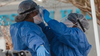 Healthcare workers from the Medical University of South Carolina clean each other's gear at a COVID-19 testing site in a parking lot