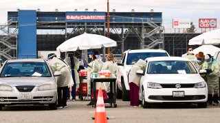In this Jan. 22, 2021, file photo, healthcare personnel dressed in personal protective gear help inoculate people arriving to receive Covid-19 vaccines at the Fairplex in Pomona, California, one of five mass COVID-19 vaccine sites opened across Los Angeles County this week.