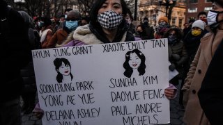A person holds a sign with the names of the people who died at a peace vigil to honor victims of attacks on Asians