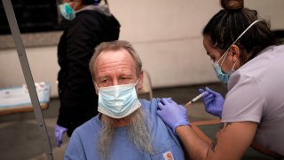In this Feb. 3, 2021, file photo, EMT Rachel Bryant, right, administers a COVID-19 vaccine to a homeless man in the courtyard of the Midnight Mission in Los Angeles. Homeless Americans who have been left off priority lists for coronavirus vaccinations — or even bumped aside as states shifted eligibility to older age groups — are finally getting their shots as vaccine supplies increase.