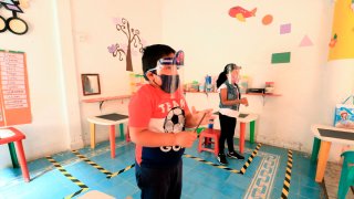 Dos niños con equipo de protección juegan en su salón de clases