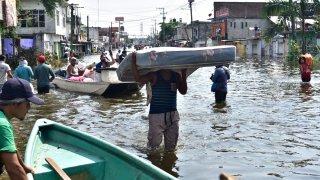 Varios hombres, uno de ellos cargando un colchón, caminan en una inundación en calles de Tabasco