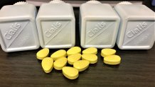 Neon green pills sit scattered on a table, in front of four plastic bottles that read "Cialis." The pills are counterfeits seized by U.S. Customs and Border Protection.