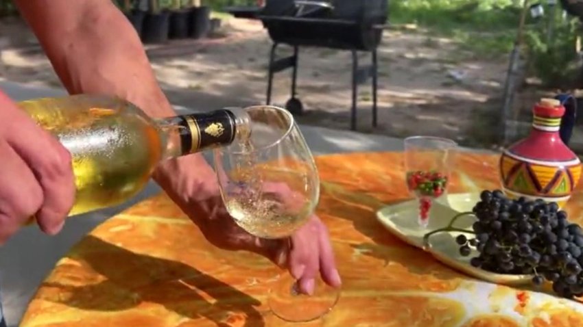 Persona sirviendo una copa de vino blanco.