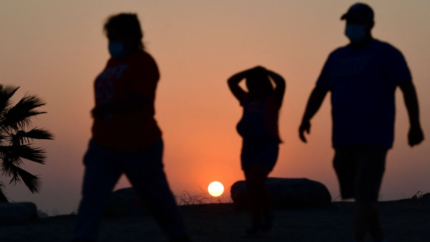 The sun sets behind people walking an afternoon hike in Los Angeles, California on July 12, 2021.