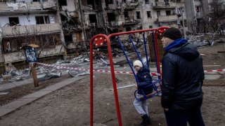 A boy plays on a swing in front of a damaged residential block hit by an early morning missile strike on Feb. 25, 2022, in Kyiv, Ukraine.