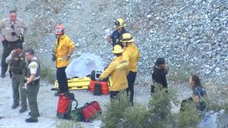 Firefighters and sheriff's deputies stand near a cliff where a man jumped into a river in Mount Baldy.