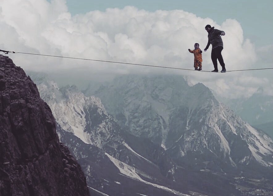 A photoshopped image of Alix and Kenny Deuss walking over a tight wire over mountain peaks.