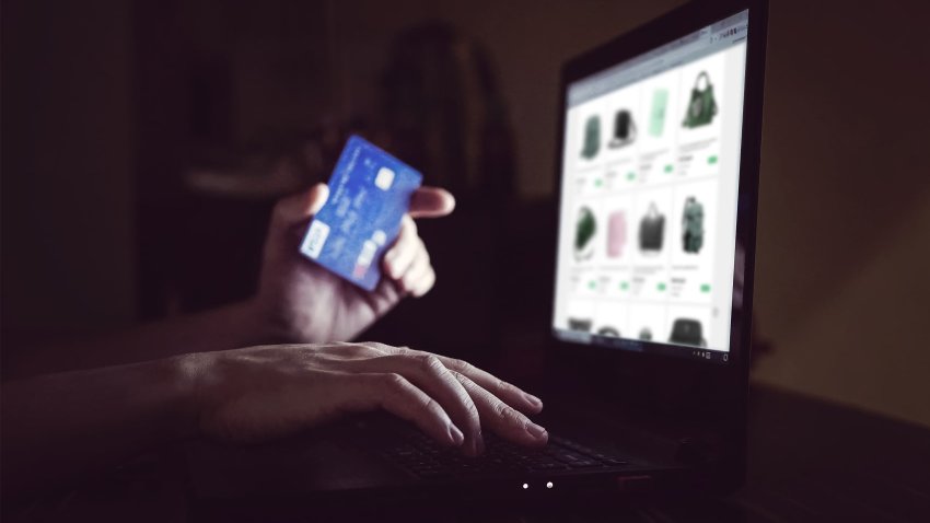 A young man holds a credit card and uses a laptop for online shopping.