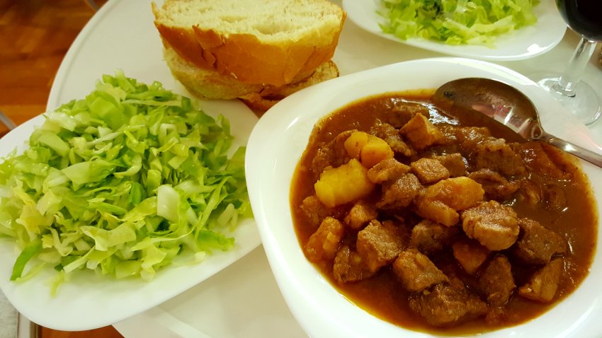 Served juicy goulash with fresh green salad and bread. White plates on a white table. A glass of wine next to a plate