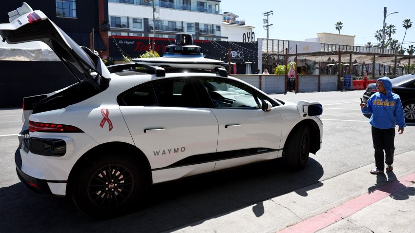 LOS ANGELES, CALIFORNIA – MARCH 14: A person takes photos of a Waymo autonomous self-driving Jaguar taxi near Venice Beach on March 14, 2024 in Los Angeles, California. Beginning today, Waymo One is offering robotaxi services in a 63-square mile area of greater Los Angeles including Santa Monica, Venice and downtown with over 50,000 people on the wait list. Waymo is owned by Alphabet, Google’s parent company.  (Photo by Mario Tama/Getty Images)