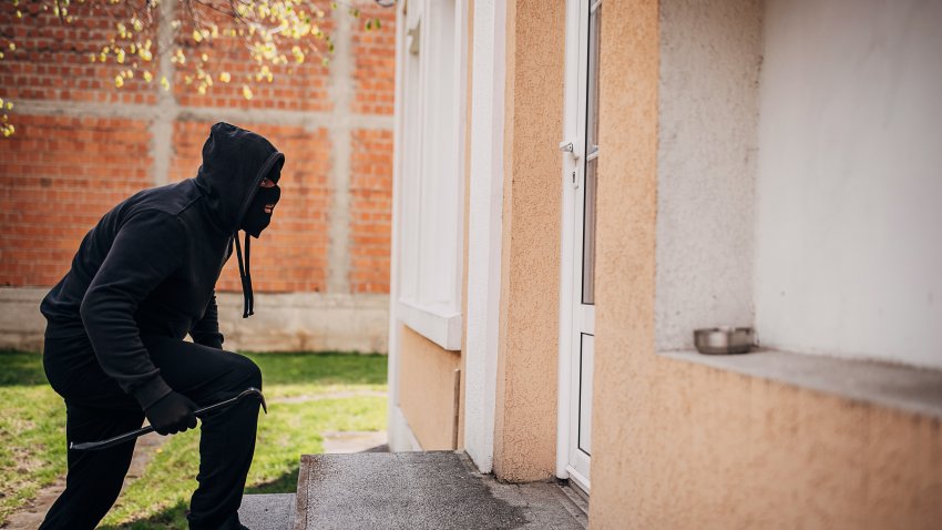 One man, criminal dressed all in black with crowbar, trying to break in house.