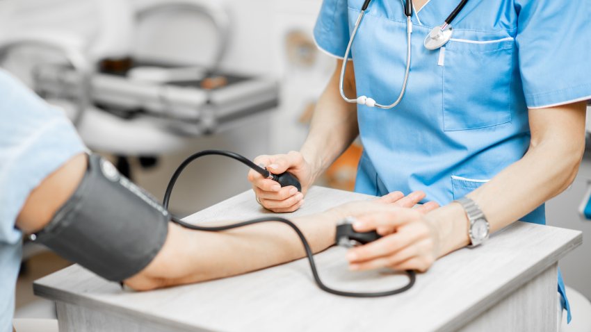 Nurse measuring blood pressure of a senior woman patient during an examination in the clinic, close-up view with no face