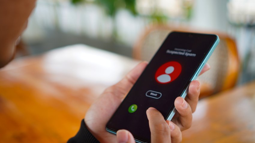 Over the shoulder view of a Man receiving an incoming suspected call from unknown caller on her smartphone and rejecting the call at home. Device screen showing warning sign as detected by the network provider. Phone scam and fraud concept