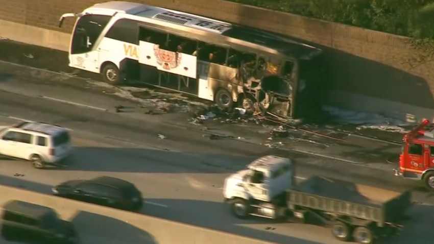The burned wreckage of a tour bus on the side of a freeway Aug. 21, 2026.