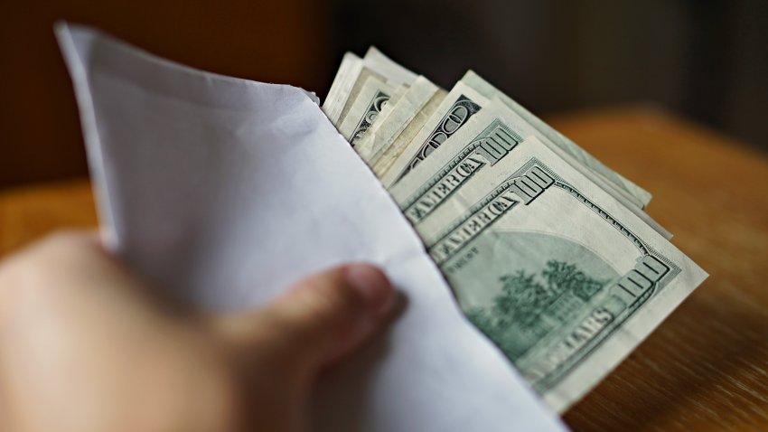 Male hand holding and passing a white envelope full of American Dollars (USD, US Dollars) as a symbol of illegal cash transfer, money laundering or bribery