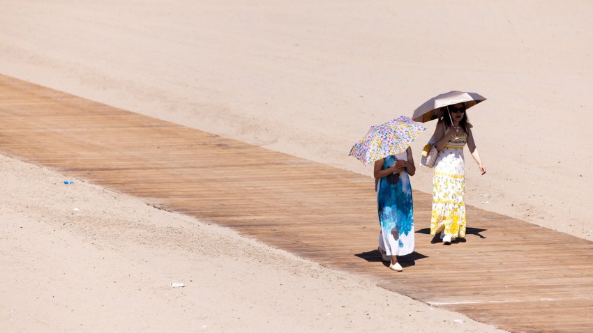 People walk with umbrellas to shade from the heat at the Santa Monica Pier.