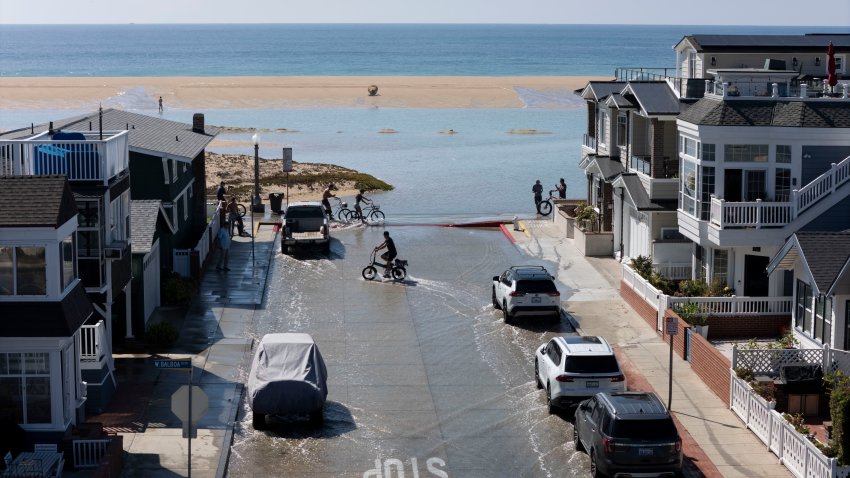 NEWPORT BEACH, CA – October 09: People cross sea water that flooded city streets at the Balboa Peninsula bike path along W. Oceanfront in Newport Beach on Friday, October 9, 2026. A hurricane swell and an overlapping south swell, combined with high tide brought flooding along the California coast. (Photo by Paul Bersebach/MediaNews Group/Orange County Register via Getty Images)